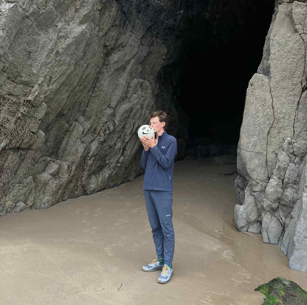 Eli küsst einen Nike-Fußball vor einer Höhle am Strand