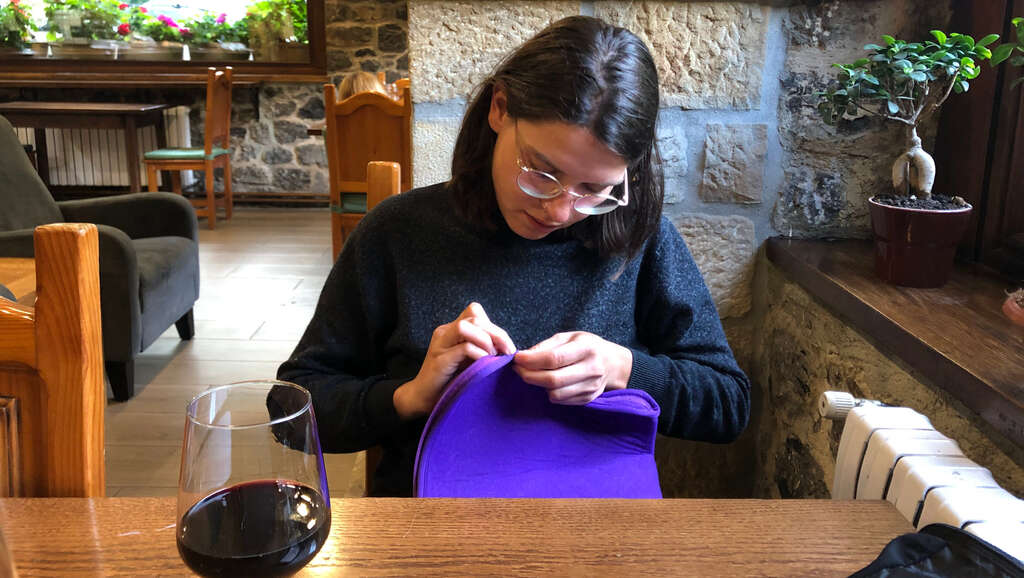 Kathi flickt ein Loch in einer Laptoptasche, am Tisch ein Glas Wein