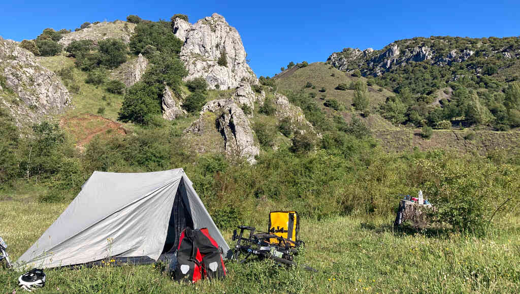 Ein Zelt steht zwischen Gestrüpp vor einem felsigen Hügel