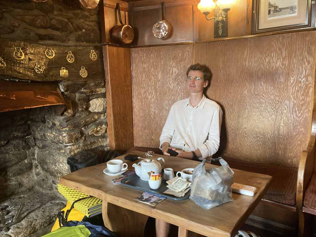 Eli sitzt in einer getäfelten Stube vor einem Tisch mit Teetablett