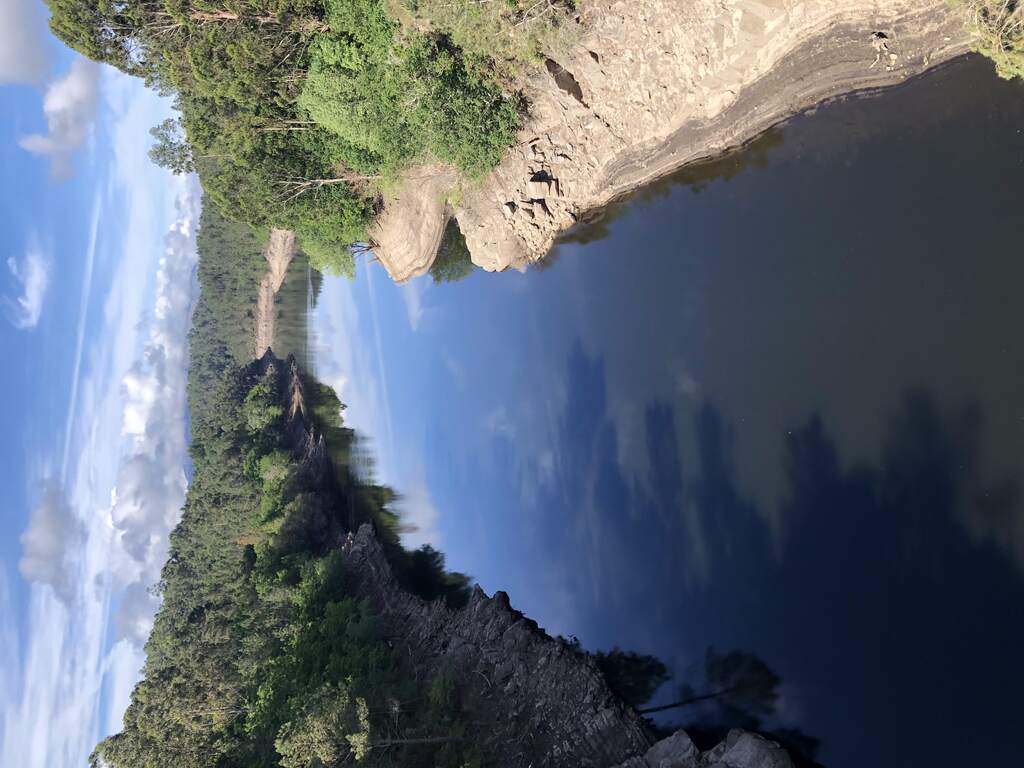 Ein spiegelglatter Fluss mit steinigem Ufer an dem sich ein wechselnder Wasserstand abzeichnet