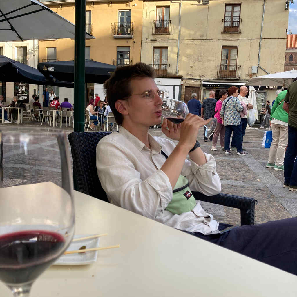 Eli trinkt in einem Schanigarten aus einem Glas Wein