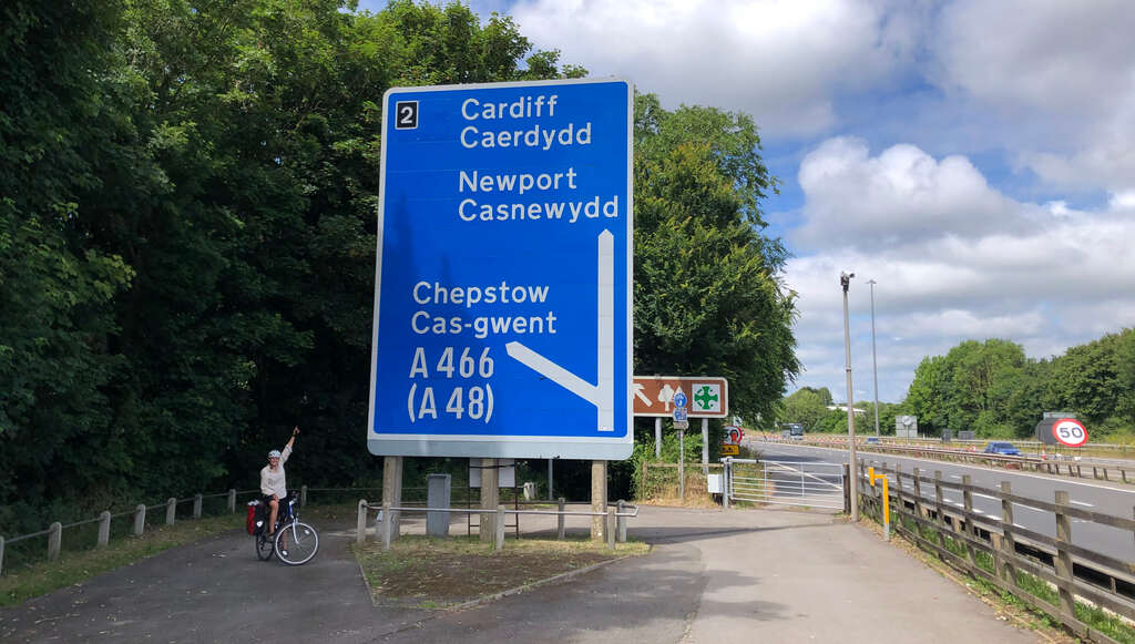 Kathi steht unter einer riesigen Autobahntafel mit Text in Englisch und Walisisch