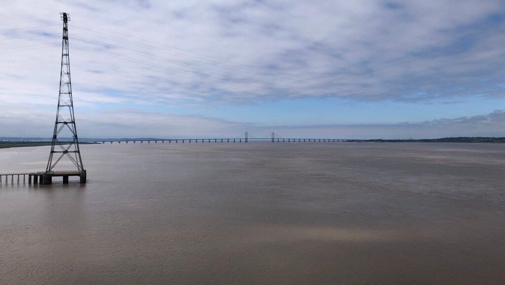 Ein breiter dreckiger Fluss aus dem ein Strommast ragt und über den am Horizont eine riesige Brücke führt