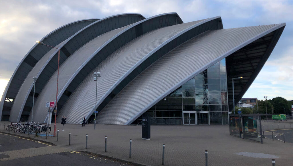 Ein Gebäude mit einer Fassade aus mehreren ineinander verschachtelter Metallflächen die nach oben hin spitz zulaufen, an der Vorderseite eine Glasfront