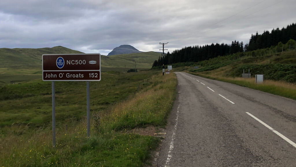 Ein Schild am Straßenrand auf dem steht 'NC500', 152 Meilen bis John O' Groats