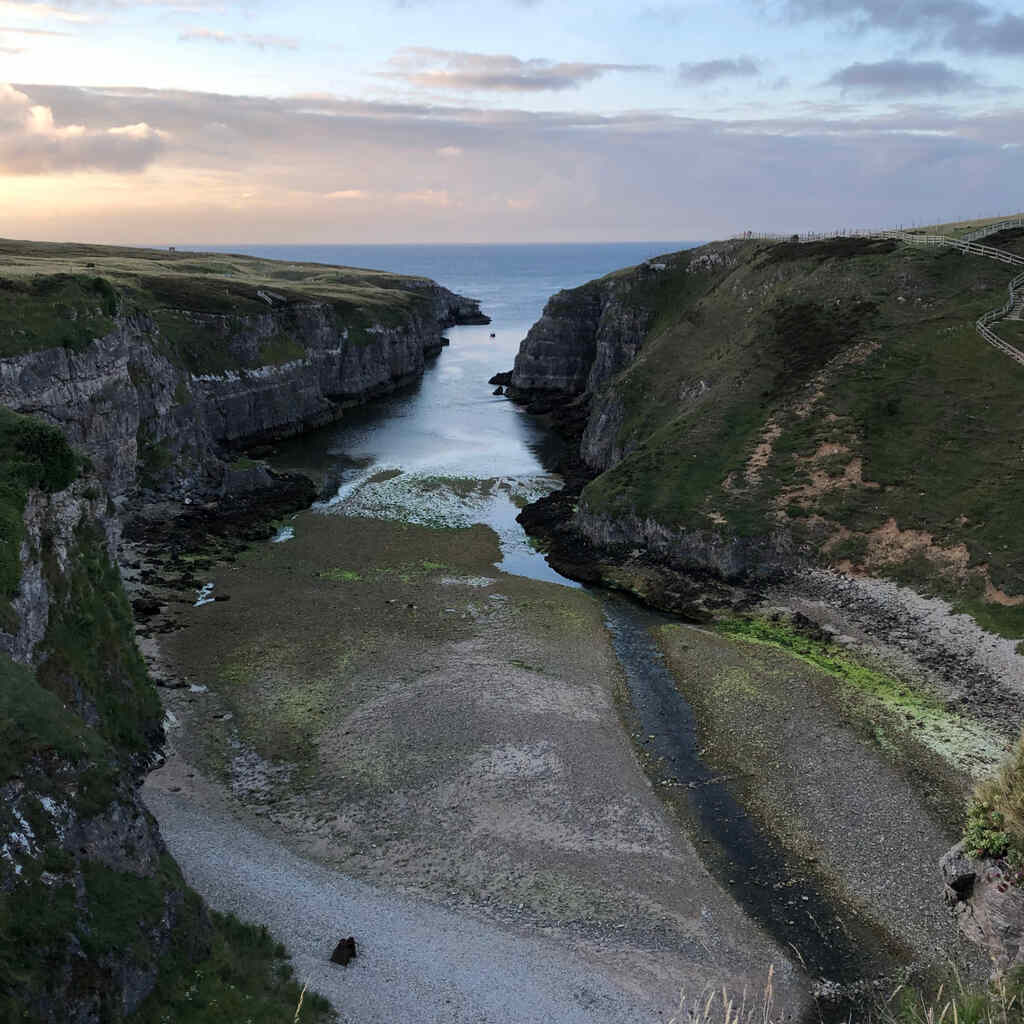 Ein enger Fjord mit Steilklippen an den Seiten, am Ende ein Kiesstrand, kurz vor Sonnenuntergang