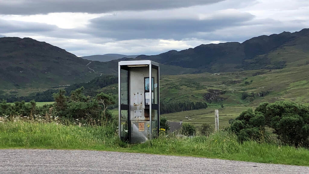 Die Reste einer Telefonzelle stehen am Straßenrand vor einer leeren bergigen Landschaft