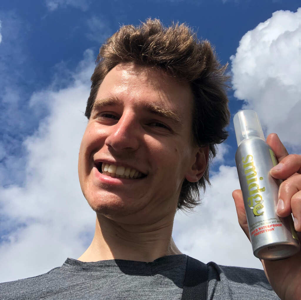 Eli schaut grinsend in die Kamera mit einer Dose Gelsenspray in der Hand