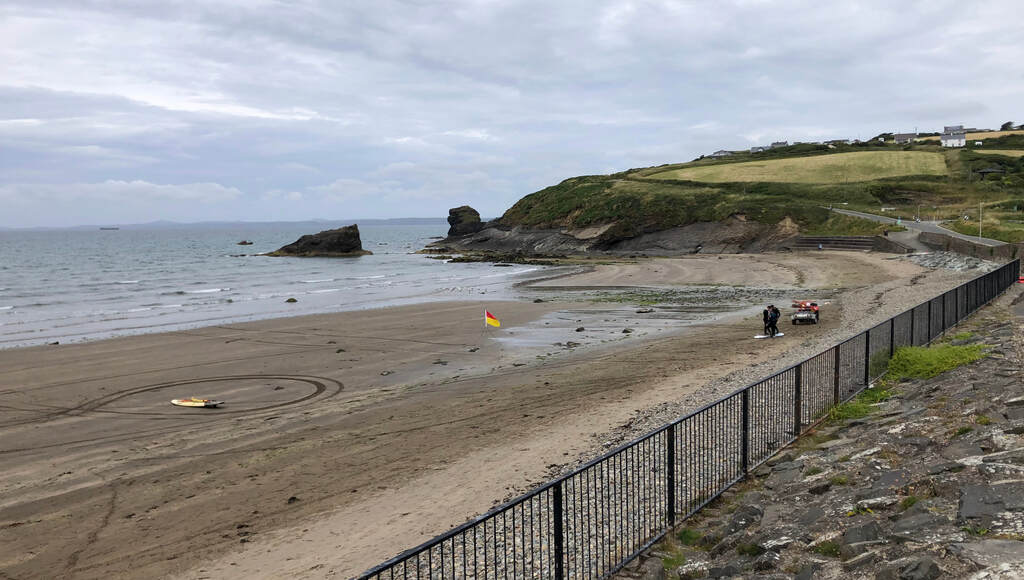 Ein breiter Strand mit ein paar Felsen die am Rand der Bucht aus dem Wasser ragen