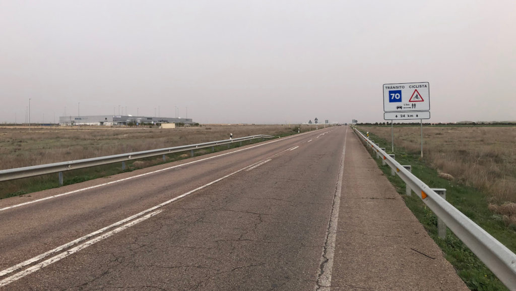 Straßenschild und Fabrik an nebliger Landstraße