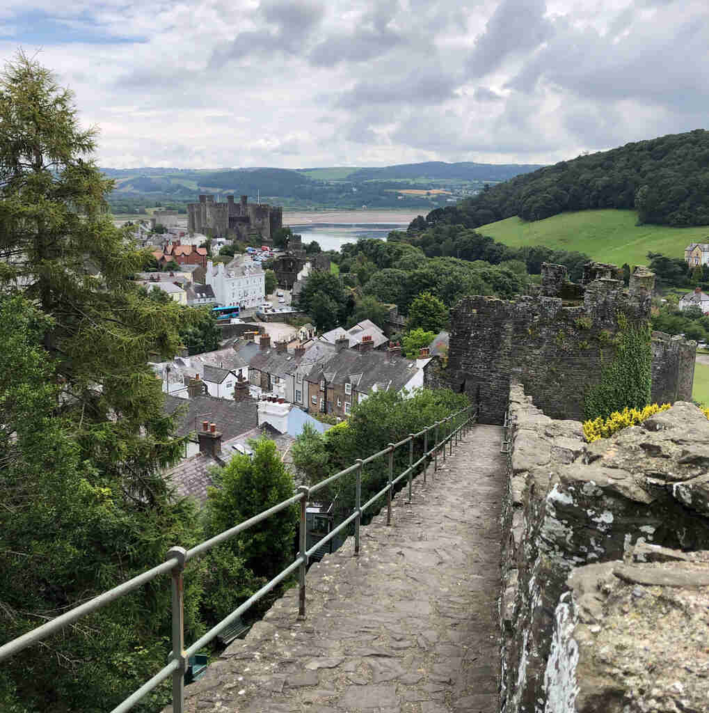 Blick von einer Mauer um eine Ortschaft auf die Ruine eines Wachturms, im Hintergrund eine mittelalterliche Burg