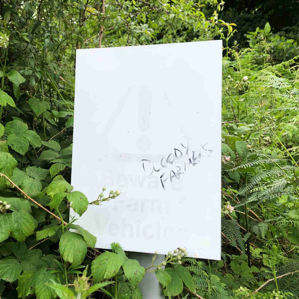 Ein ausgeblichenes Schild auf dem steht 'Beware Farm Vehicles', dazugekritzelt 'Bloody Farmers'