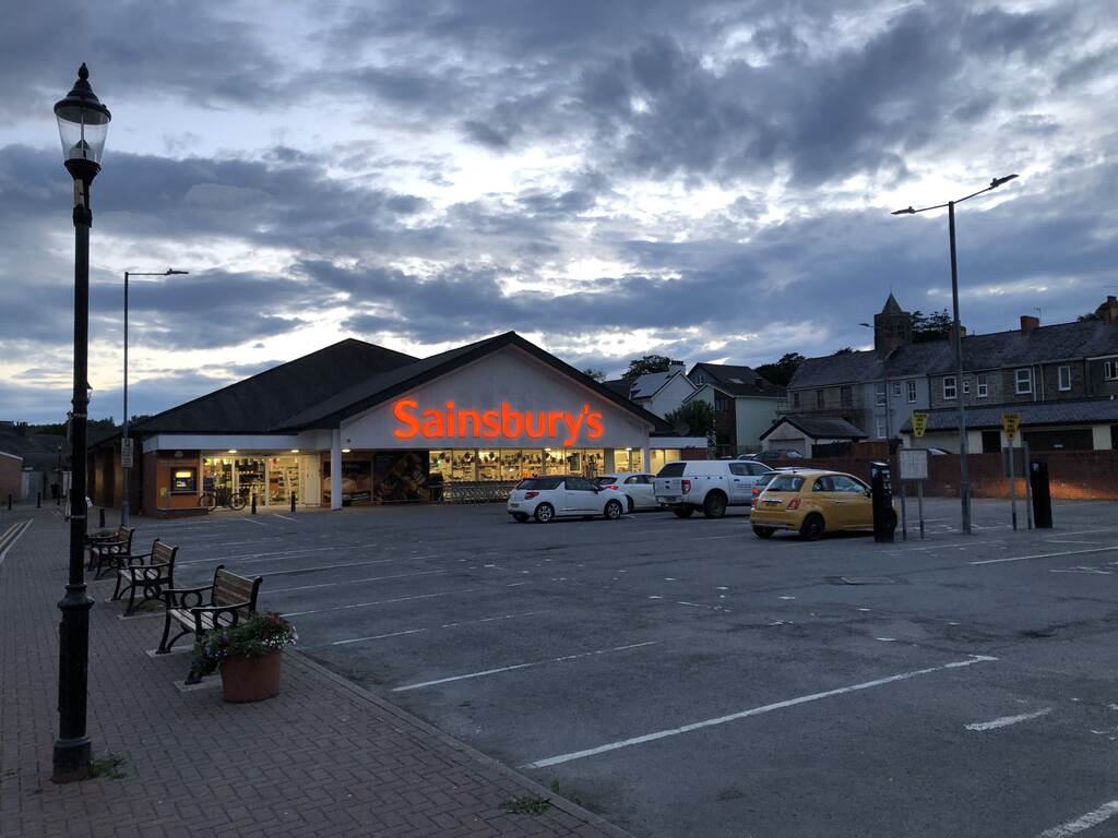 Ein fast leerer Parkplatz vor einem Sainsbury's mit großen rot leuchtenden Lettern über dem Eingang