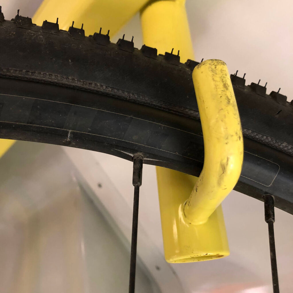 Nahaufnahme einer Fahrradfelge auf einem gelben Haken, die Felge ist um die Speiche eingerissen