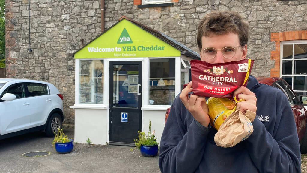 Eli steht vorm YHA in Cheddar mit einer Packung Cathedral Cheddar