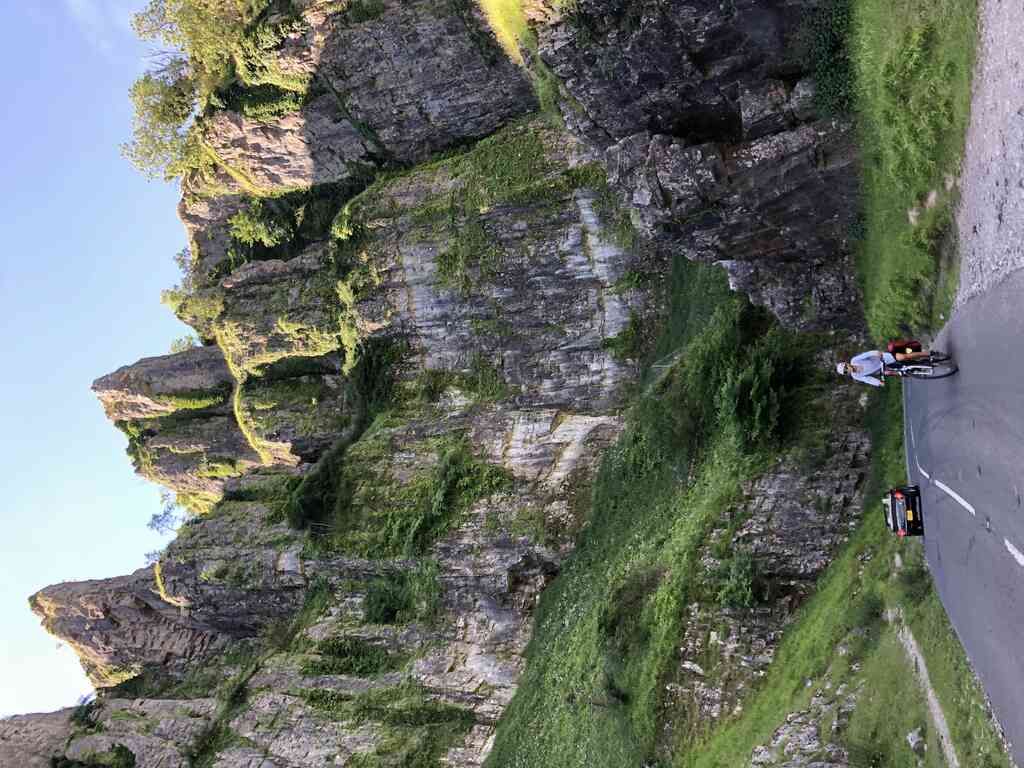 Kathi radlt eine steile Straße hoch, im Hintergrund hohe Felsen