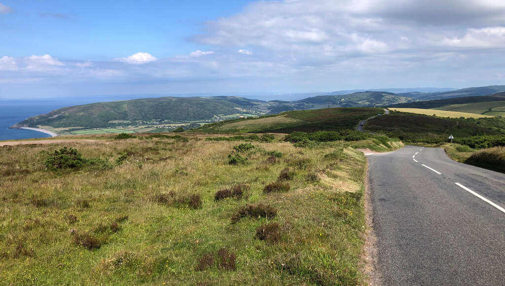 Eine Straße auf einer Hügelkuppe führt nach unten, im Hintergrund das Meer