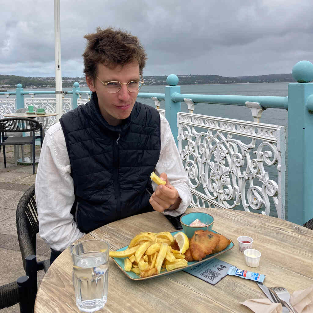 Eli sitzt an einem Tisch und isst einen Teller fish'n'chips