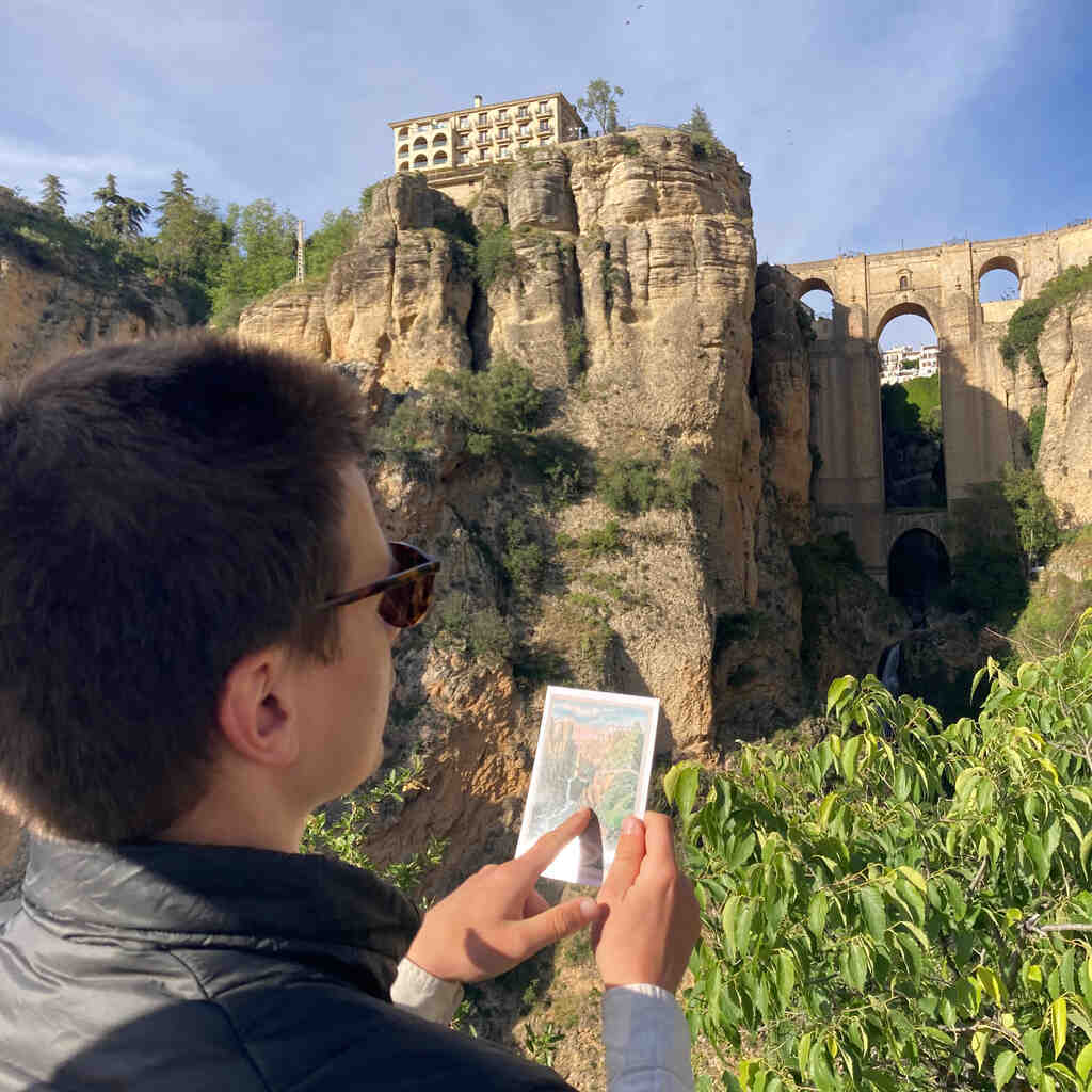 Eli blickt auf darstellende Postkarte vor dem Puente Nuevo