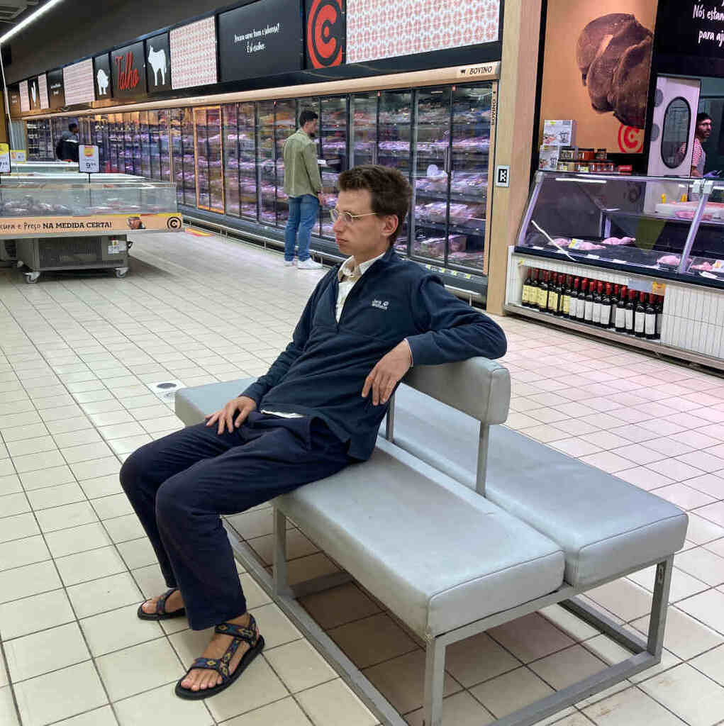 Eli sitzt auf einem Bankerl im Supermarkt