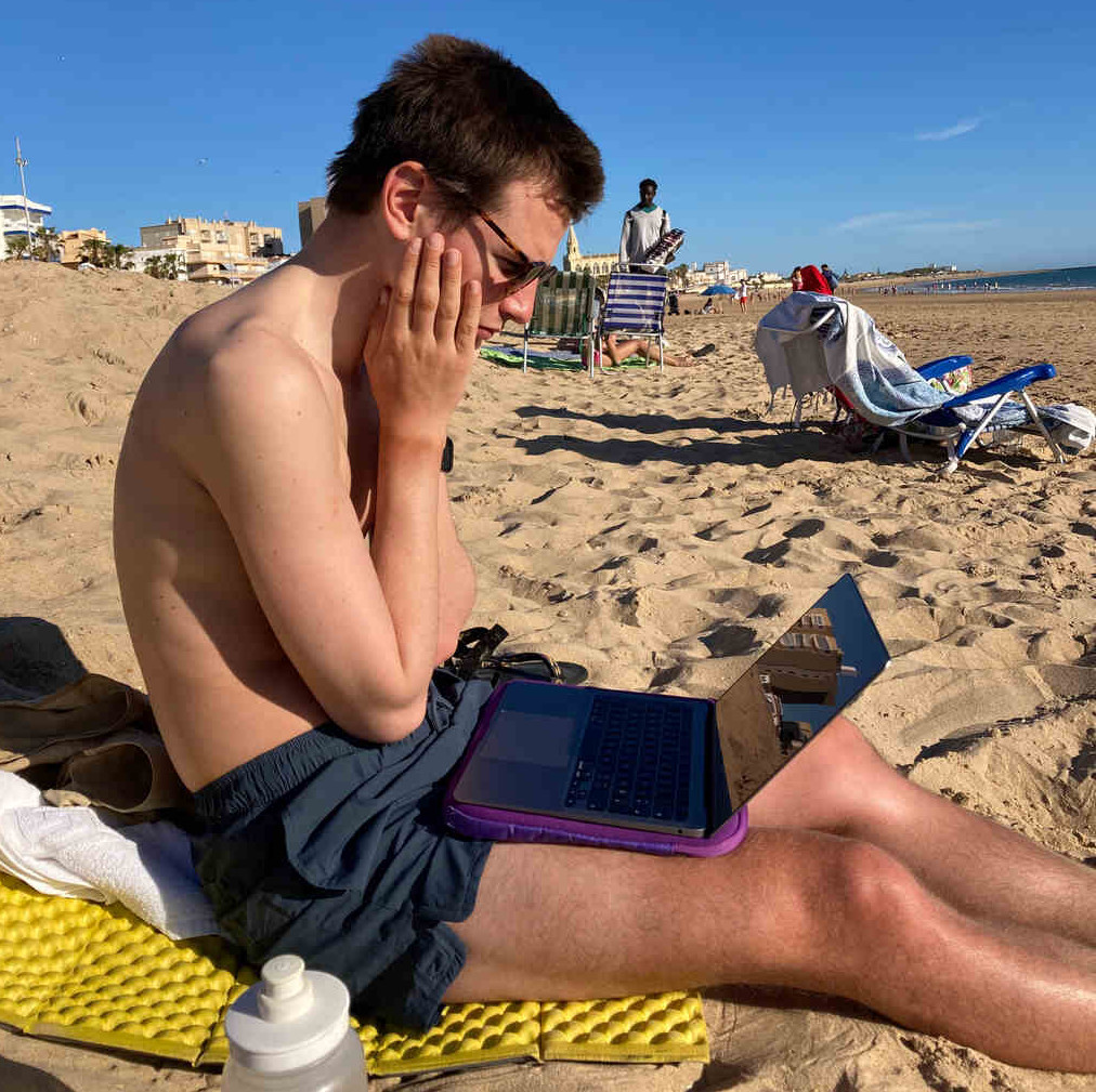 Eli sitzt am Strand in Chipiona mit dem Macbook auf dem Schoß