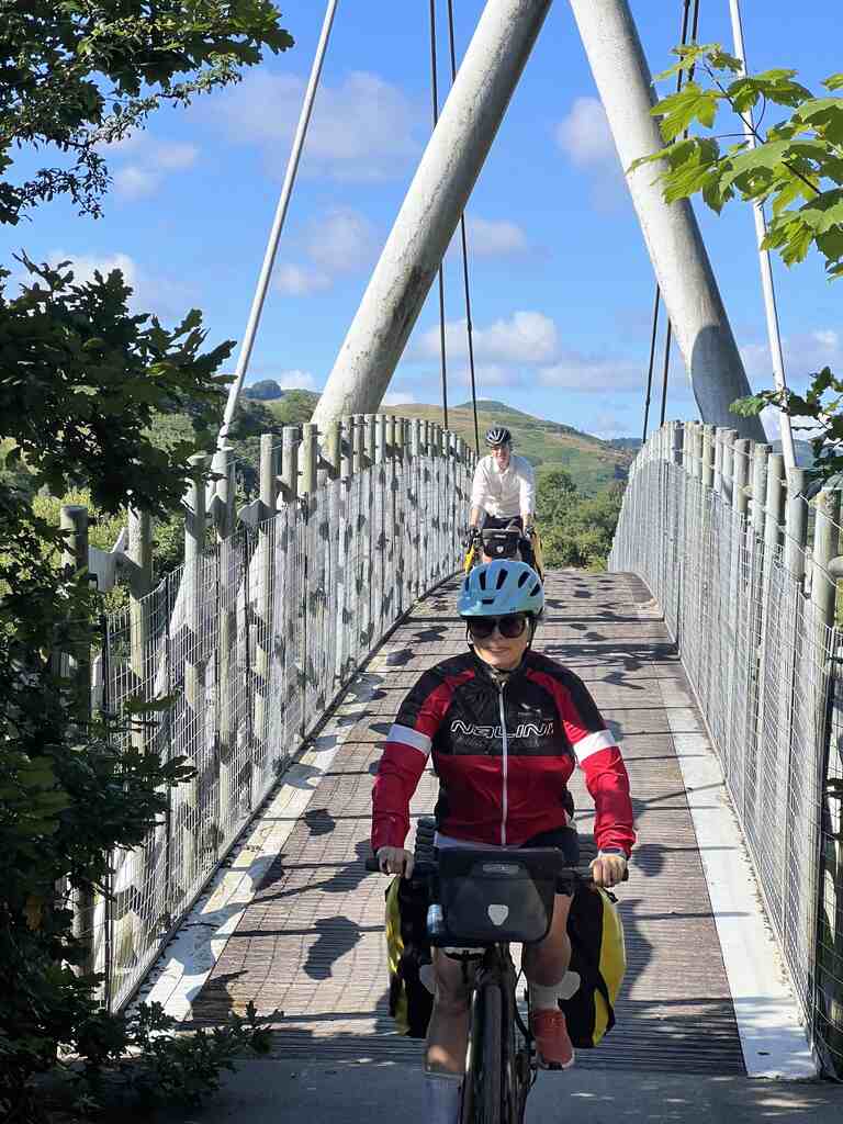 Hristina kommt von einer Brücke runter, Eli folgt dahinter, im Hintergrund nackte Hügel