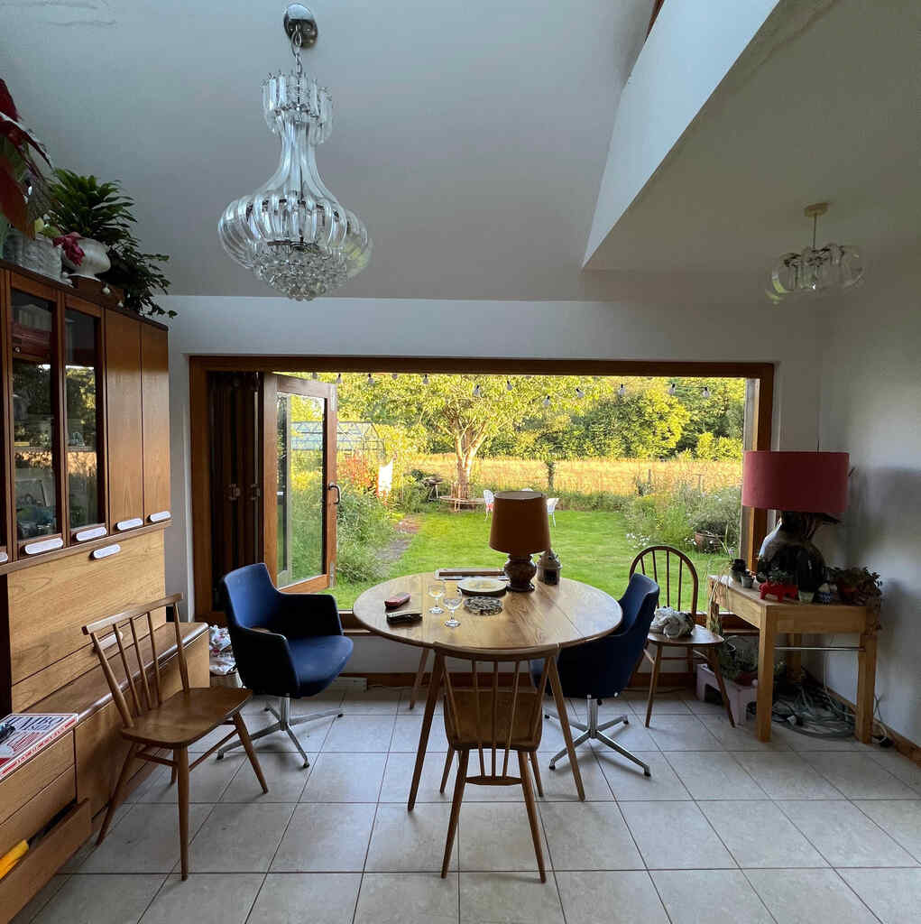 Ein gefliestes Wohnzimmer mit rundem Esstisch und einem großen faltbaren Fenster in einen Garten