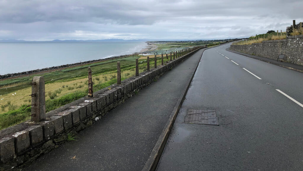 Eine nasse leere Straße überm Meer, im Hintergrund eine weite Bucht