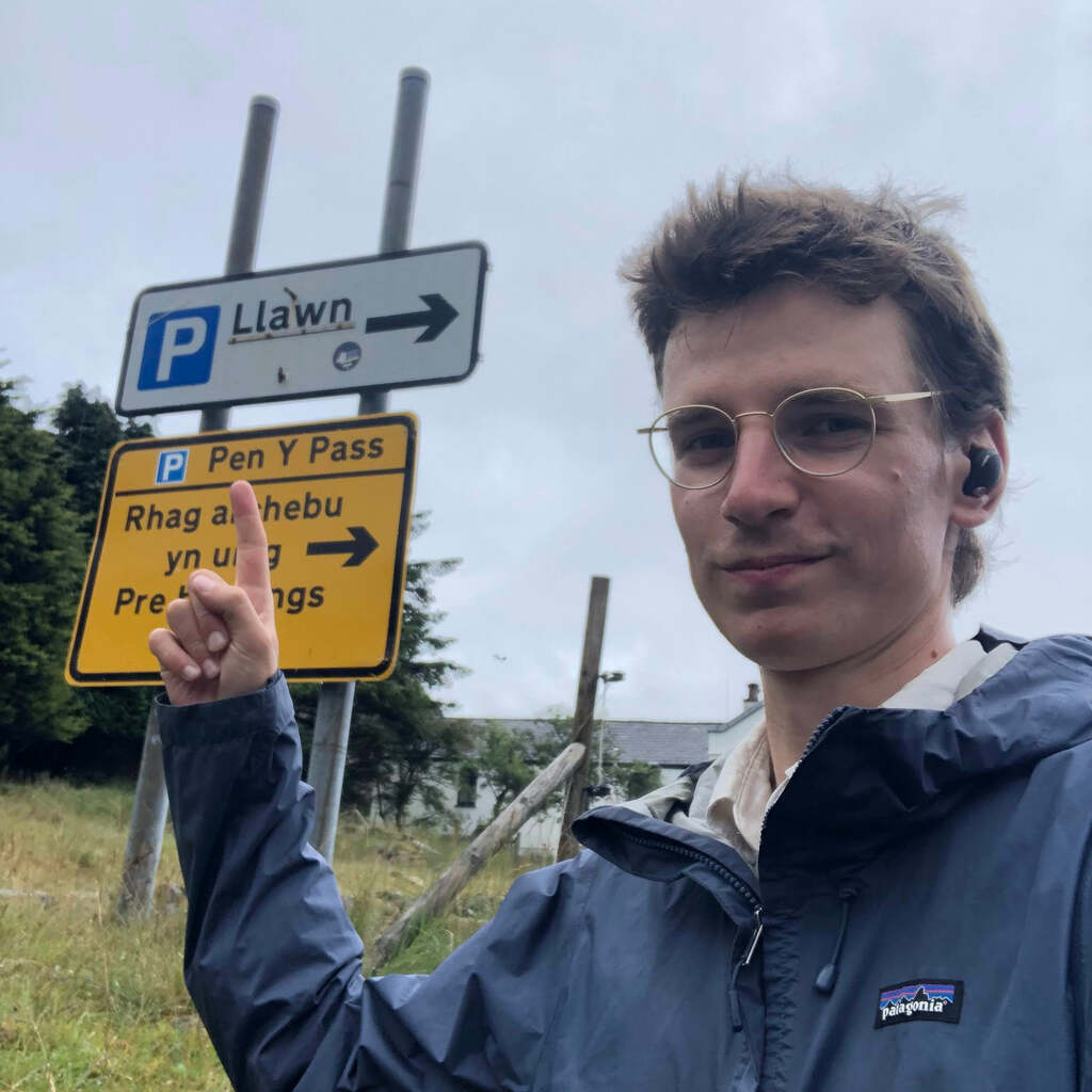 Selfie von Eli der auf ein Straßenschild zeigt auf dem der Parkplatz am Pen-y-pas angeschrieben ist