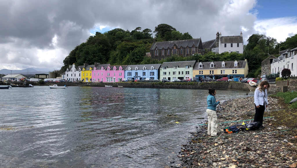 Zwei junge Frauen an einem Kiesstrand, im Hintergrund eine bunte Häuserreihe