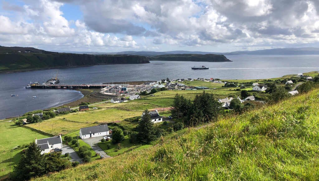 Ein kleiner Ort am Meer mit Fährhafen, eine Fähre am Weg dorthin, im Hintergrund Steilklippen