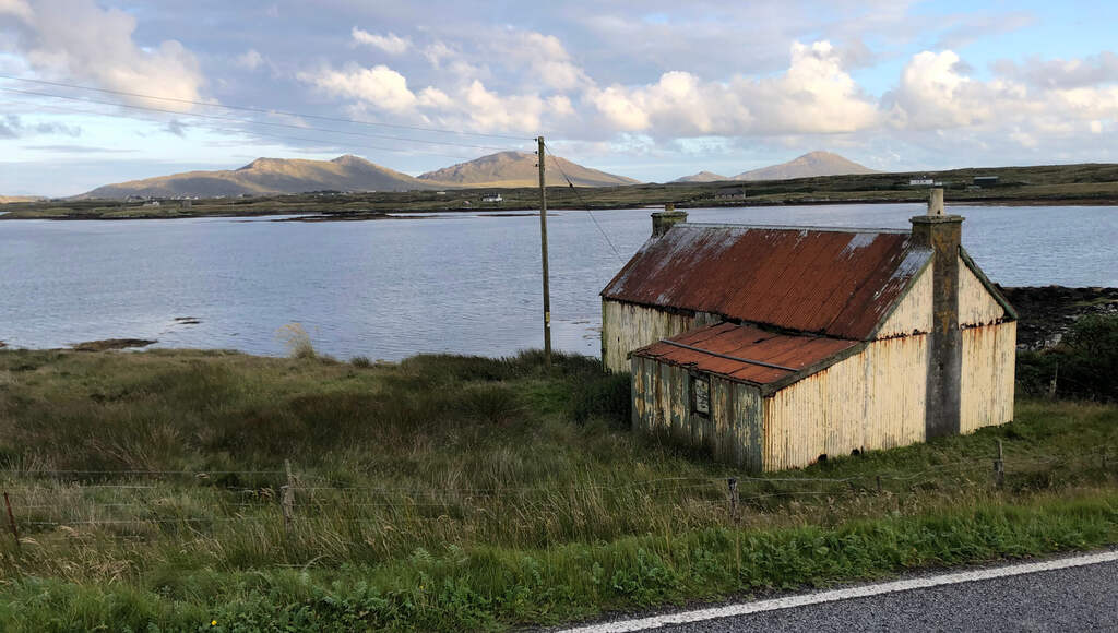 Eine rostige Wellblechhütte am Meer, im Hintergrund Berge in der Abendsonne